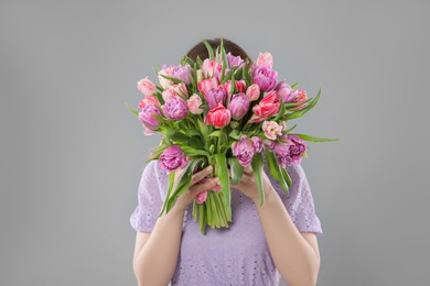 Photo of Woman covering her face with bouquet of beautiful tulips on grey background