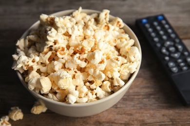 Photo of Bowl of popcorn and TV remote on wooden background. Watching cinema