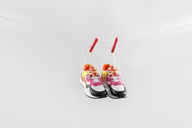 Stylish sneakers drying on washing line against light grey background