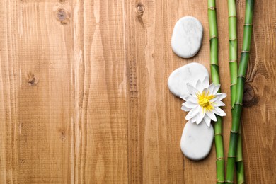 Photo of Spa stones, flower and bamboo stems on wooden table, flat lay. Space for text