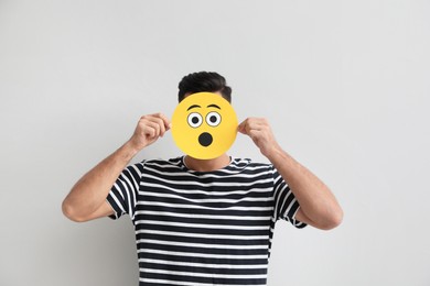 Photo of Man hiding emotions using card with drawn surprised face on white background