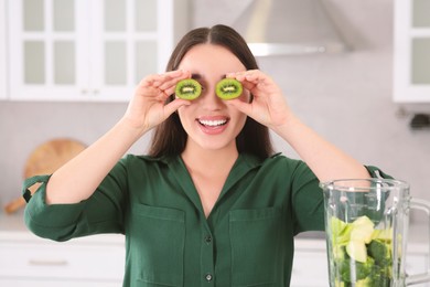 Photo of Young woman with cut kiwi for smoothie in kitchen