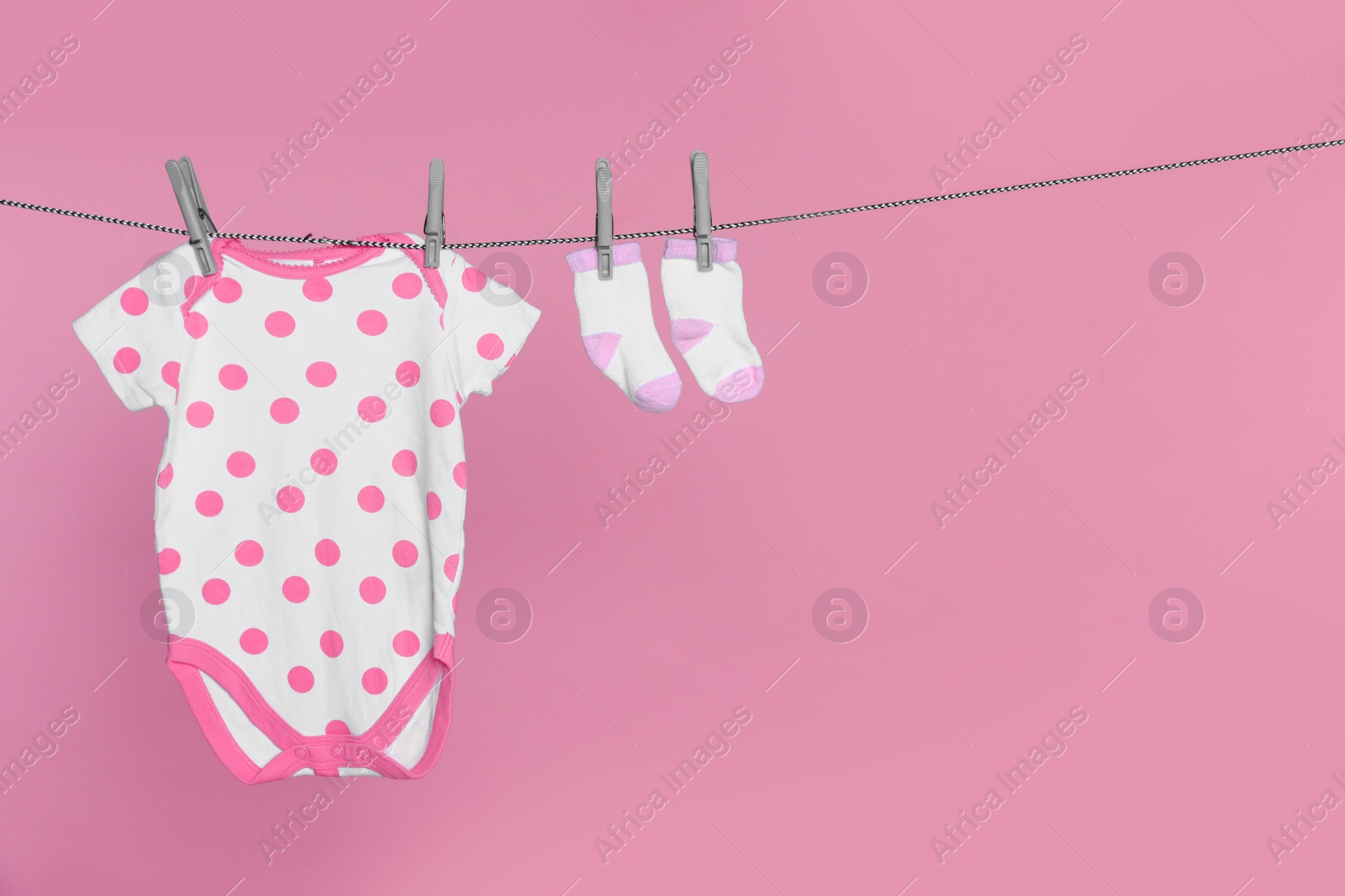 Photo of Baby onesie and socks drying on laundry line against pink background, space for text