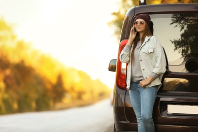 Photo of Young woman with mobile phone near car on country road. Space for text