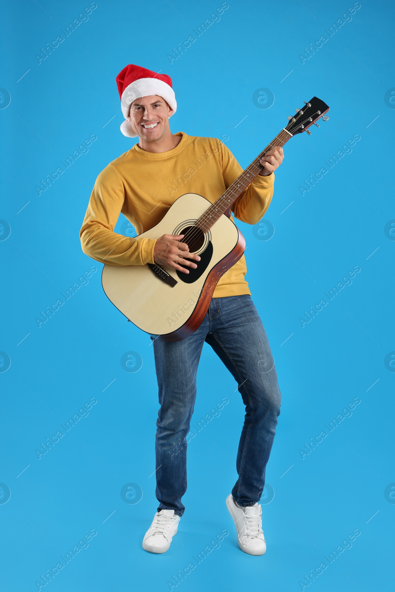 Photo of Man in Santa hat playing acoustic guitar on light blue background. Christmas music