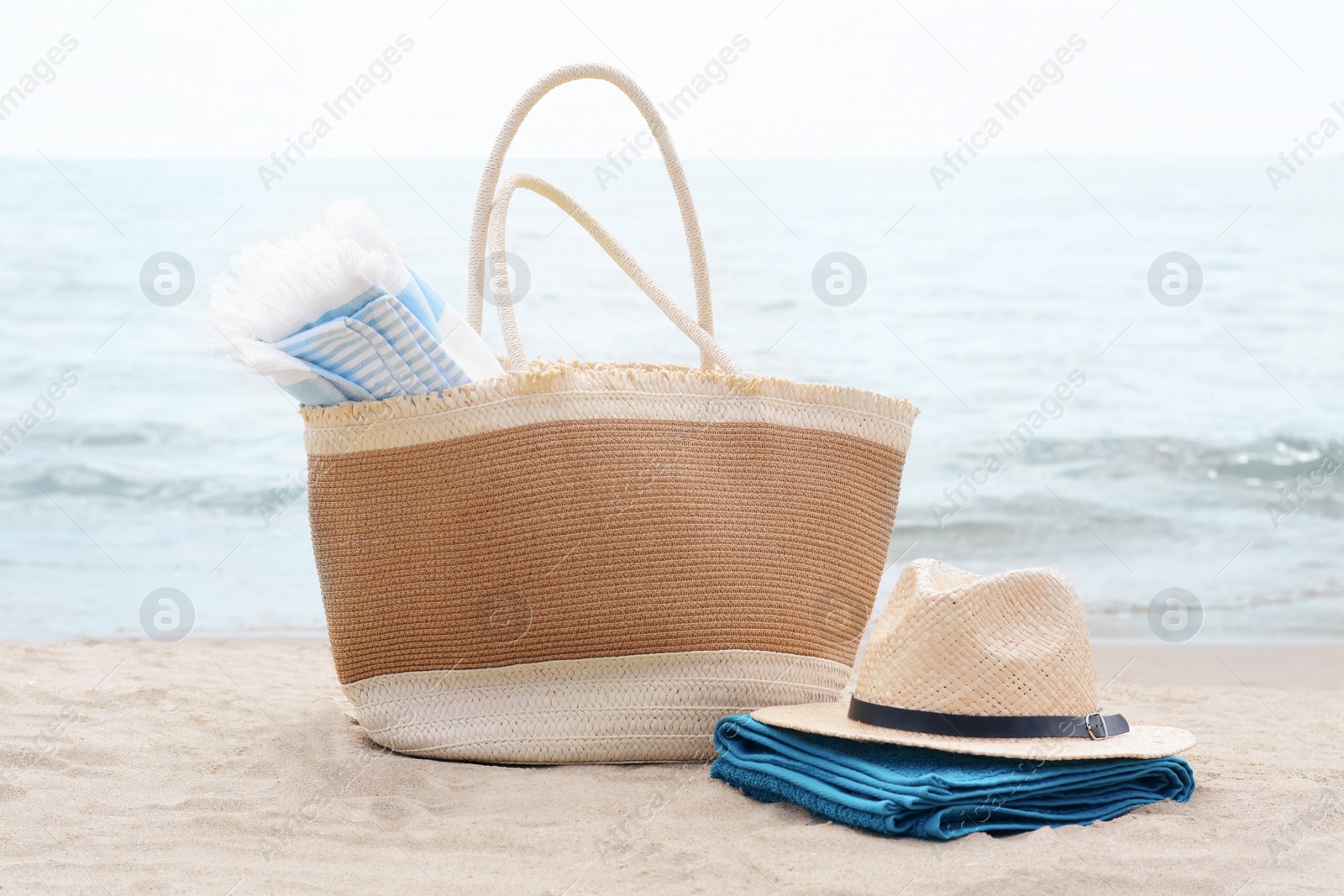 Photo of Bag with blanket, beach towel and straw hat on sandy seashore