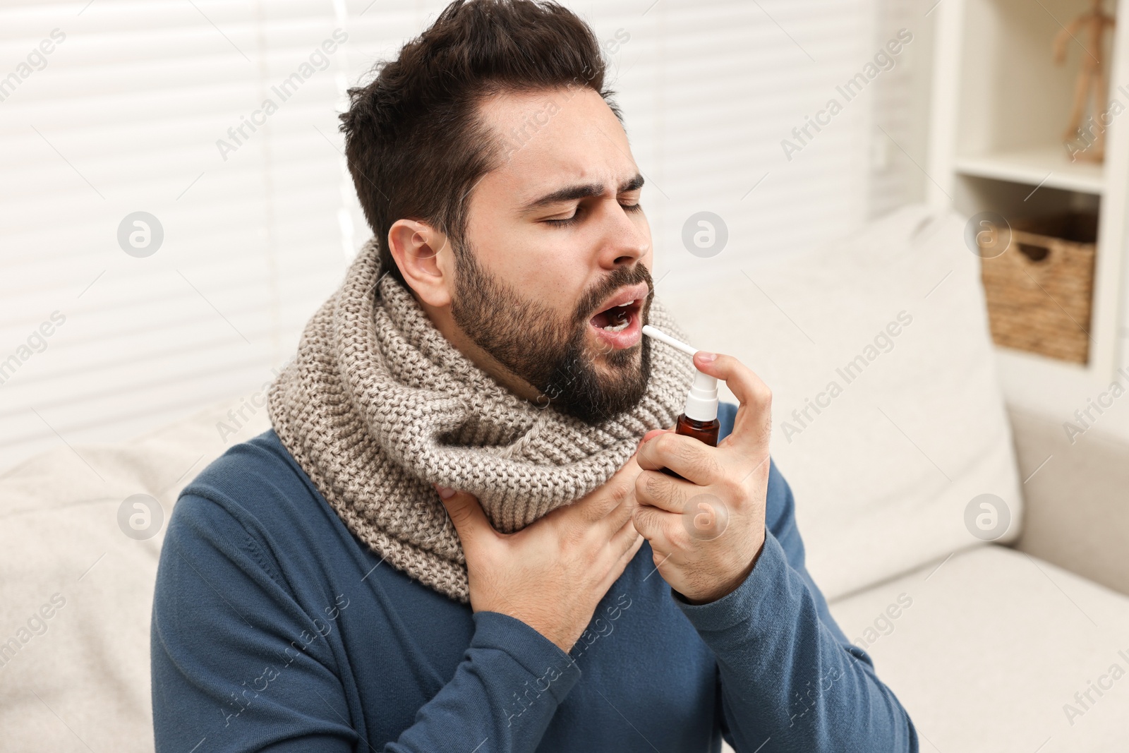 Photo of Young man with scarf using throat spray indoors