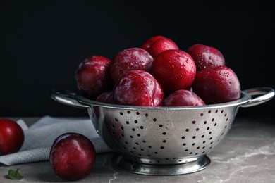 Delicious ripe plums in colander on grey marble table
