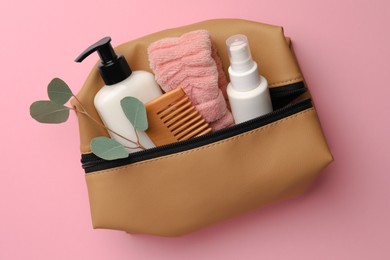 Photo of Preparation for spa. Compact toiletry bag with different cosmetic products and branch on pink background, top view