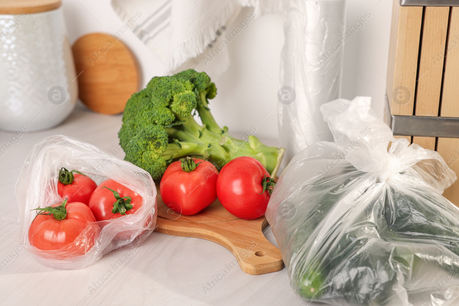 Photo of Plastic bags and fresh vegetables on white table