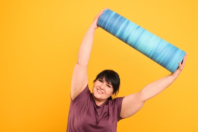 Happy overweight mature woman with yoga mat on orange background