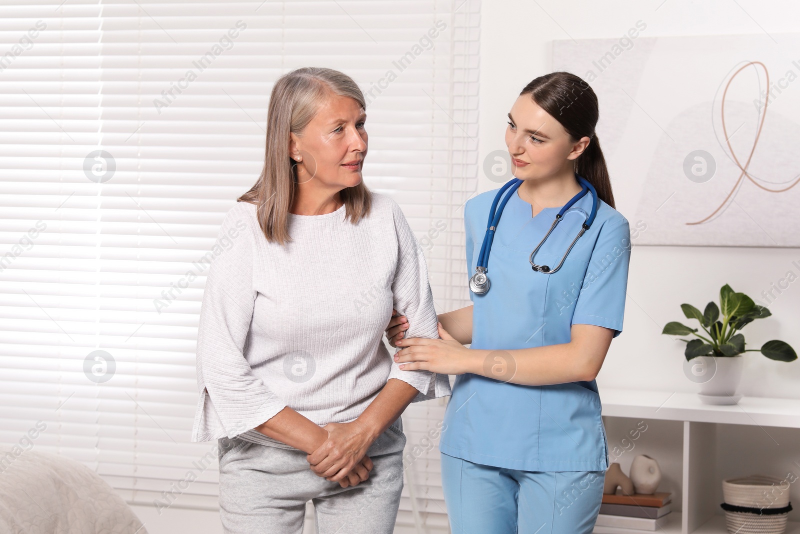 Photo of Young healthcare worker assisting senior woman indoors