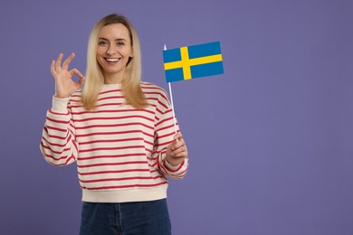 Happy young woman with flag of Sweden showing OK gesture on purple background