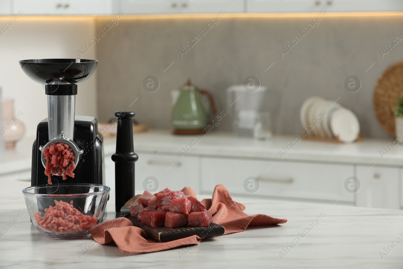 Photo of Electric meat grinder with beef mince on white table in kitchen, space for text