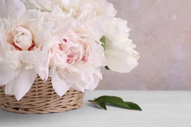Photo of Beautiful peonies in wicker basket on white table, closeup. Space for text