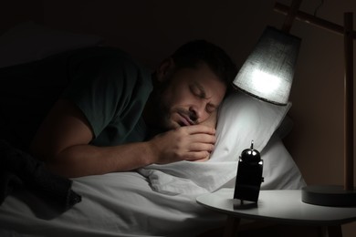 Man sleeping in bed and alarm clock on nightstand at home