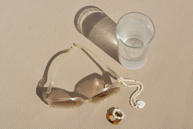 Photo of Stylish sunglasses, glass of water and jewelry on grey surface, above view