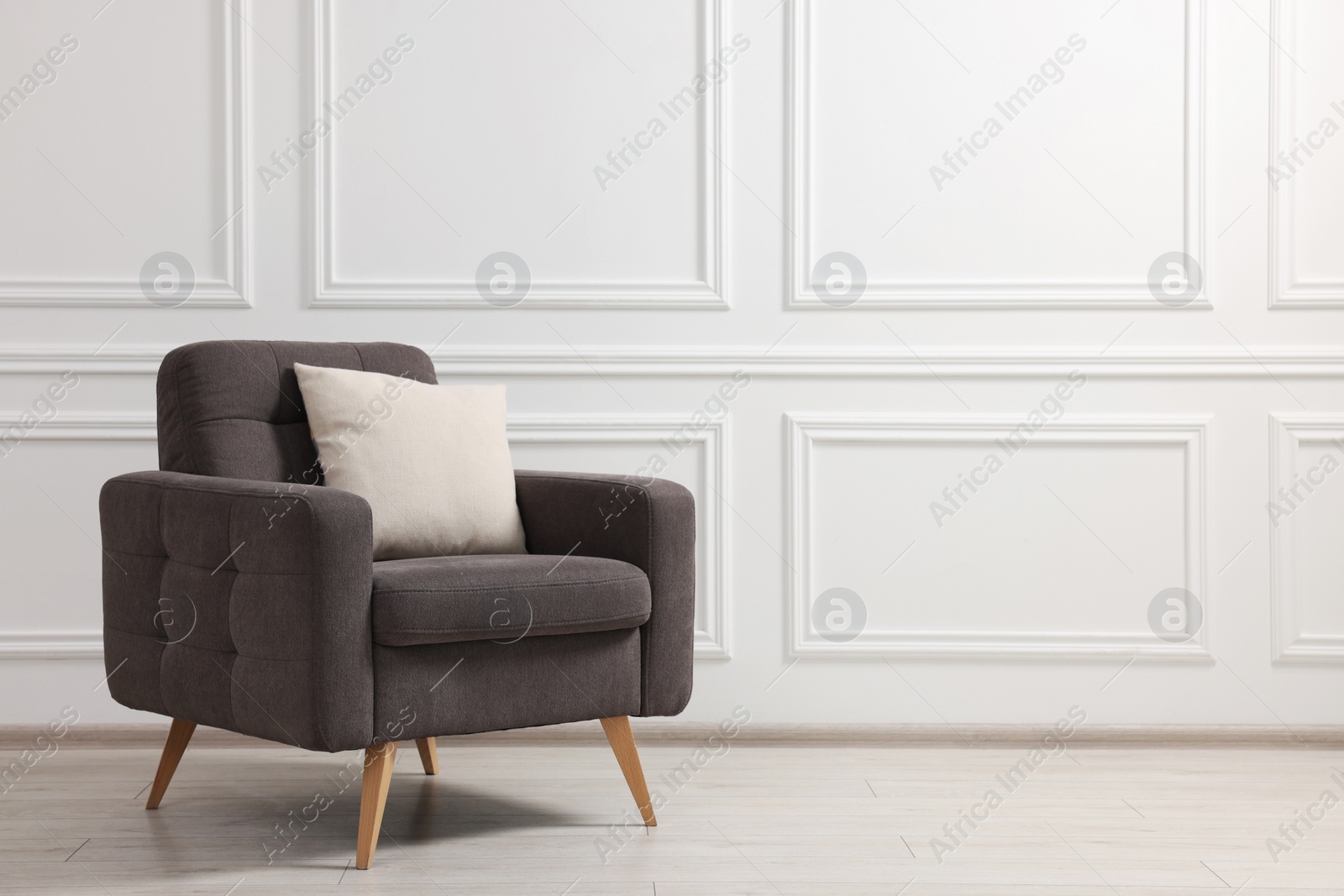 Photo of Stylish armchair with cushion near white wall indoors, space for text