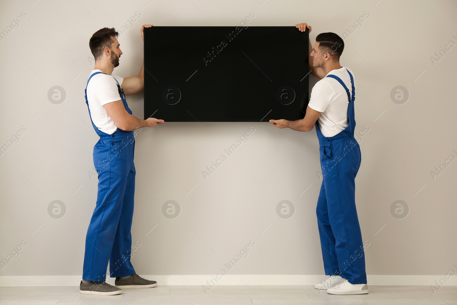 Photo of Professional technicians installing modern flat screen TV on wall indoors