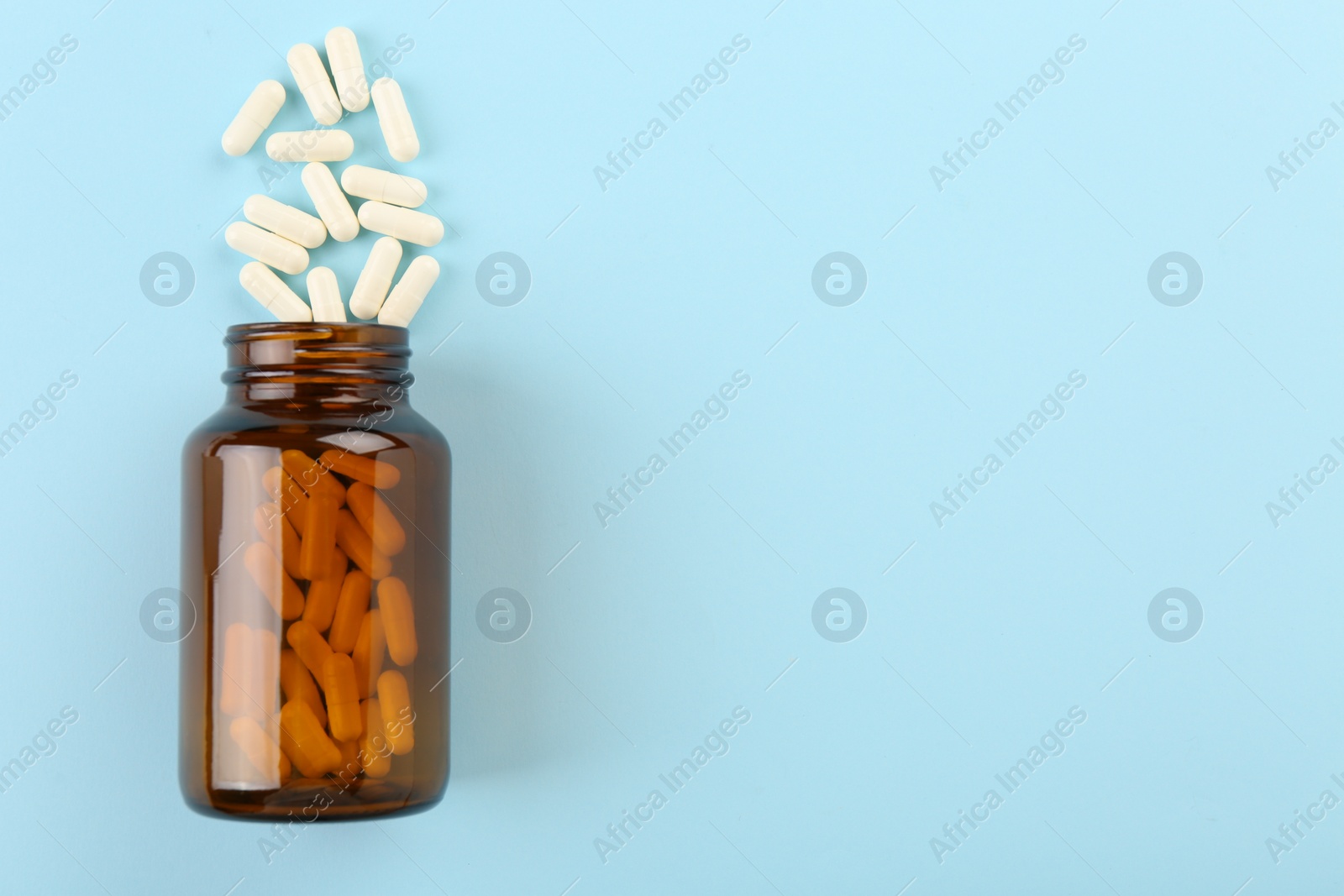 Photo of Bottle and vitamin capsules on light blue background, top view. Space for text