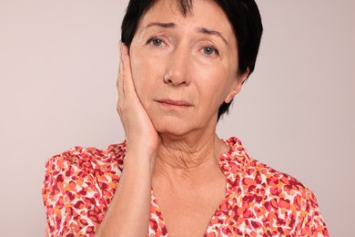 Senior woman suffering from ear pain on light grey background, closeup