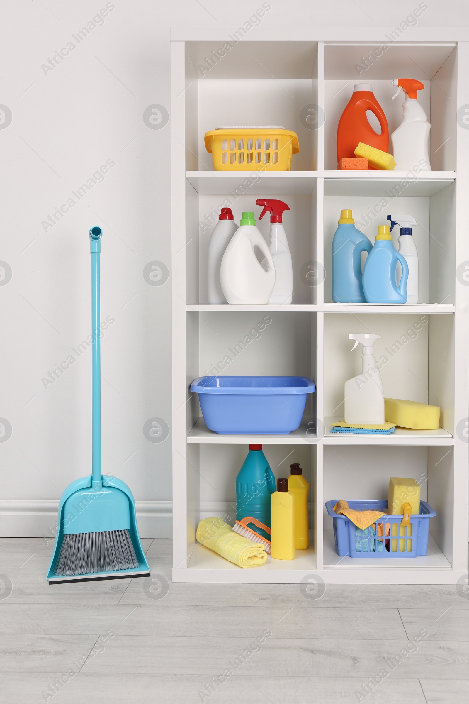 Photo of Shelving unit with detergents and cleaning tools near white wall indoors