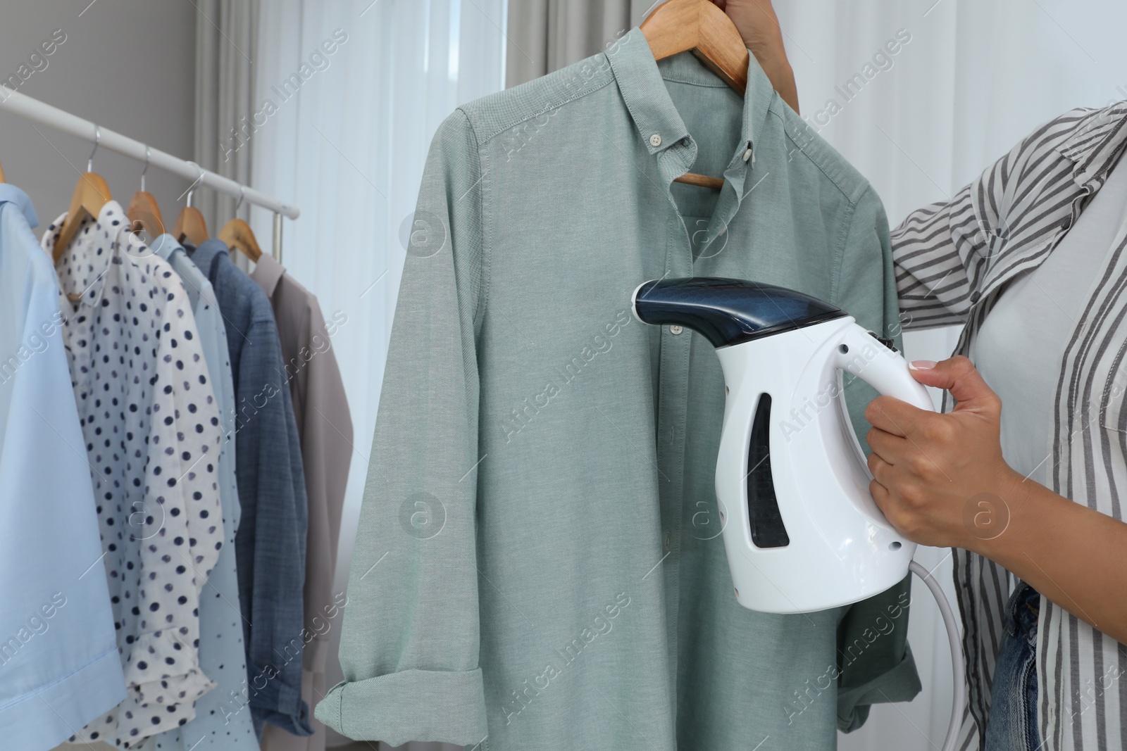 Photo of Woman steaming shirt on hanger at home, closeup