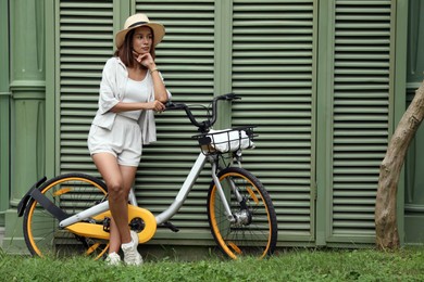 Beautiful young woman with bicycle near green wall outdoors. Space for text