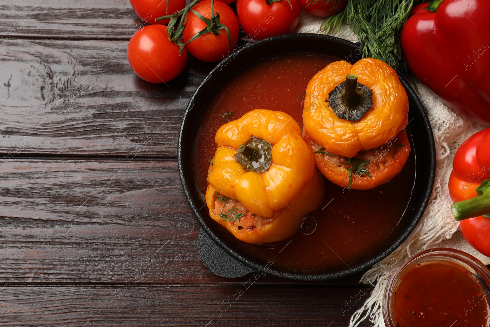 Photo of Tasty stuffed peppers in pan, sauce and products on wooden table, flat lay. Space for text