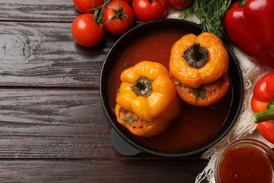 Photo of Tasty stuffed peppers in pan, sauce and products on wooden table, flat lay. Space for text