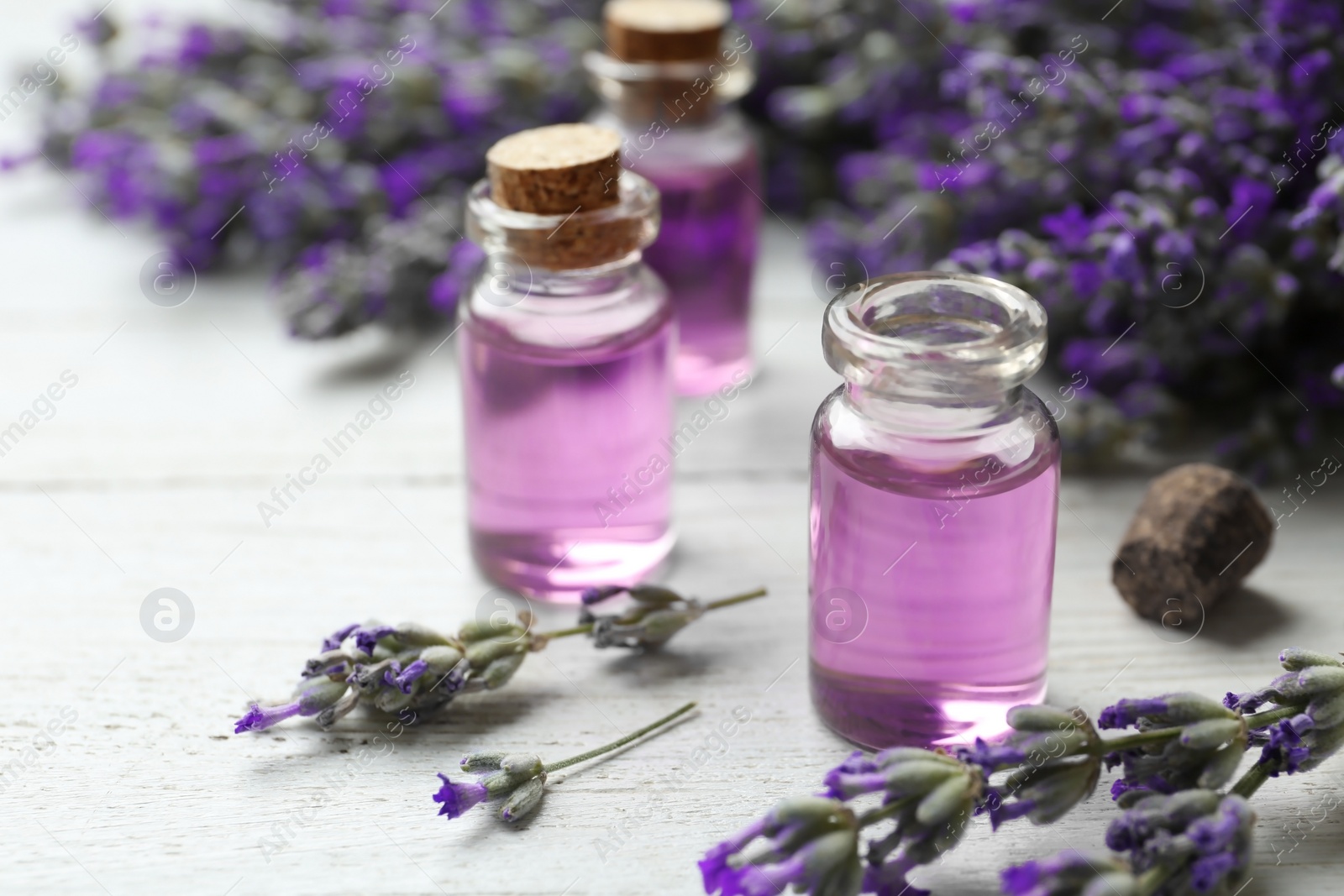 Photo of Bottles with essential oil and lavender flowers on white wooden table