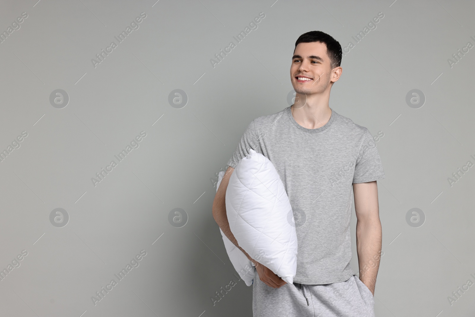 Photo of Happy man in pyjama holding pillow on grey background, space for text