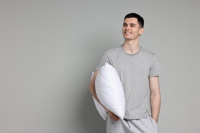 Photo of Happy man in pyjama holding pillow on grey background, space for text