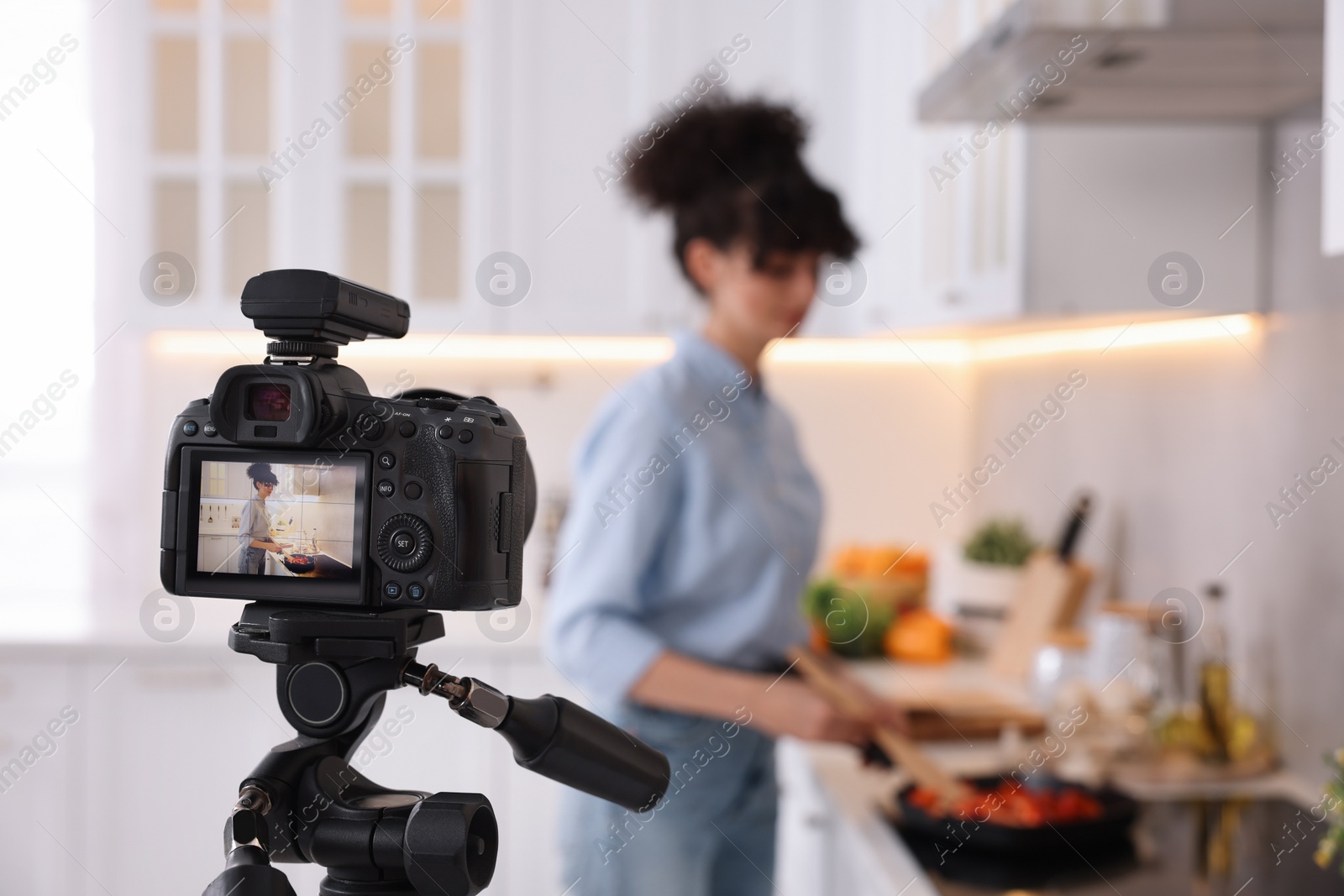 Photo of Food blogger cooking while recording video in kitchen, focus on camera