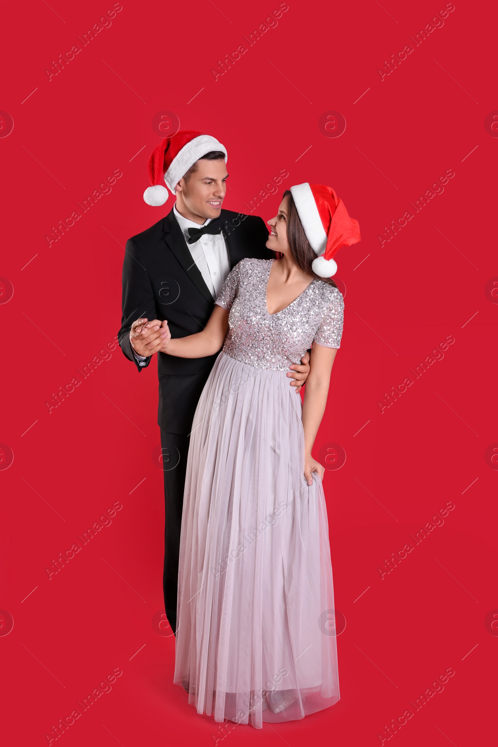 Photo of Beautiful happy couple in Christmas hats on red background