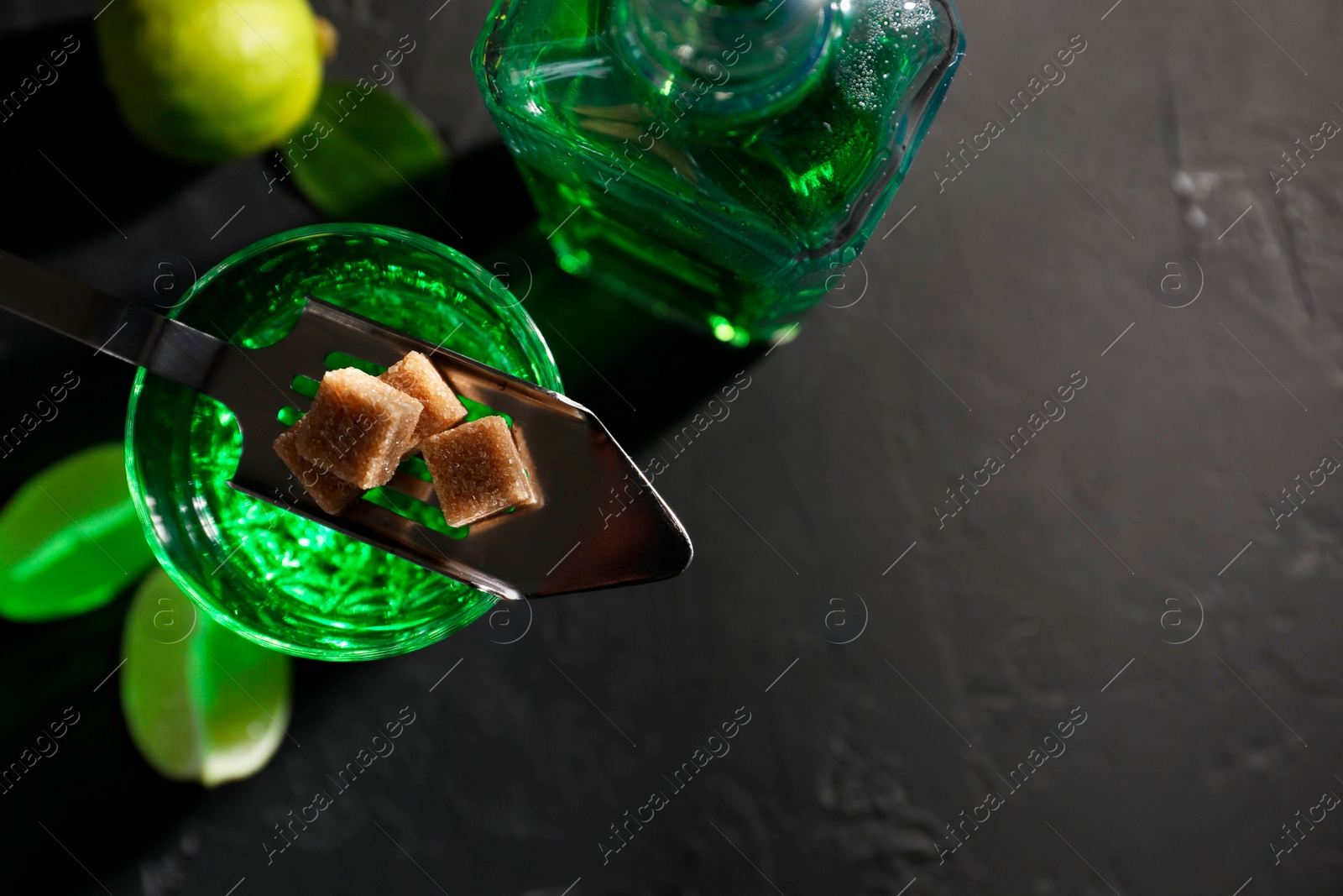 Photo of Absinthe, spoon, brown sugar and lime on black table, top view with space for text. Alcoholic drink