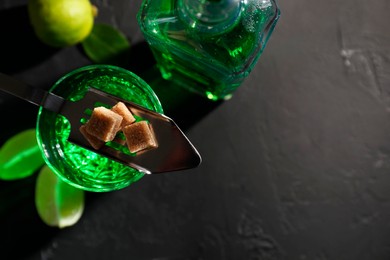 Photo of Absinthe, spoon, brown sugar and lime on black table, top view with space for text. Alcoholic drink