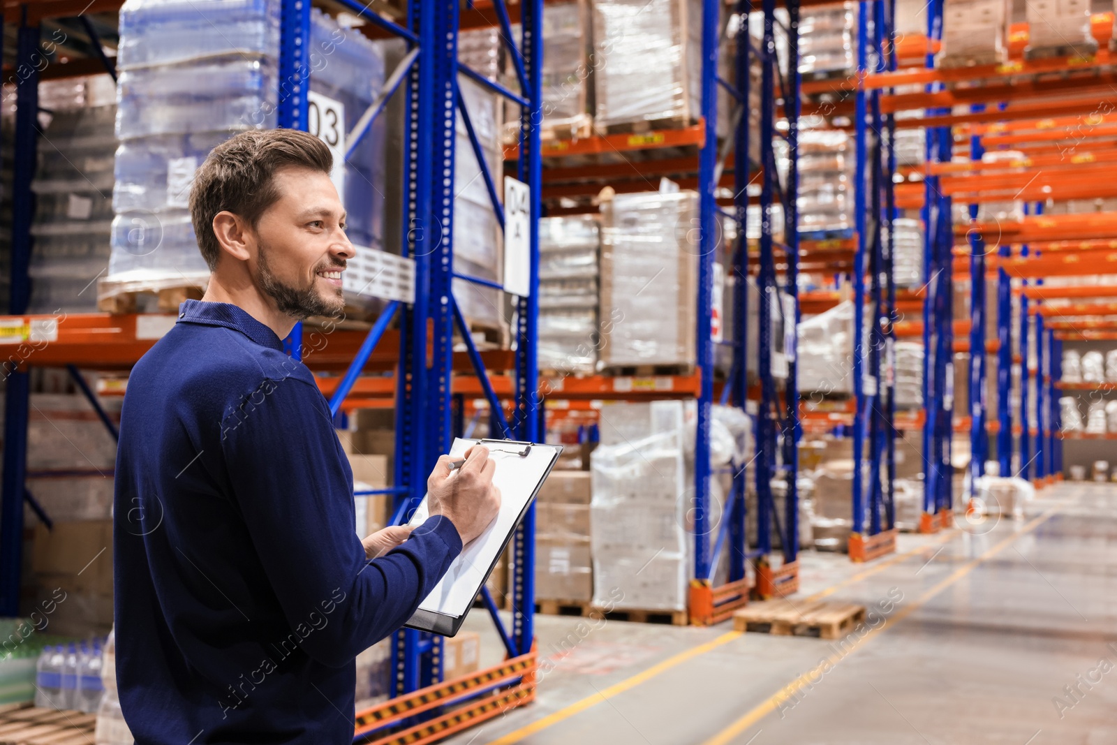 Photo of Happy manager holding clipboard in warehouse with lots of products. Space for text