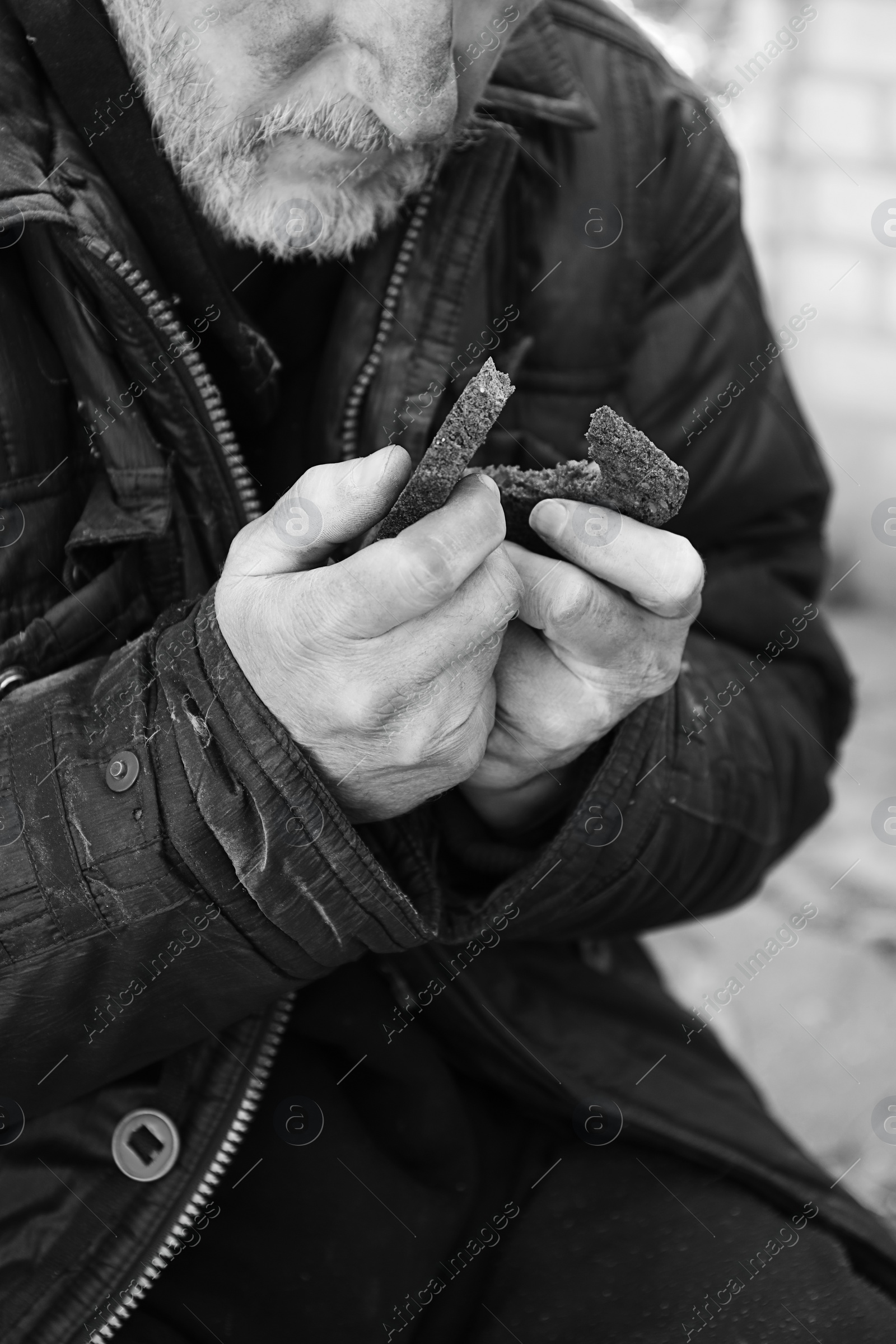 Photo of Poor homeless man holding piece of bread outdoors, closeup. Black and white effect