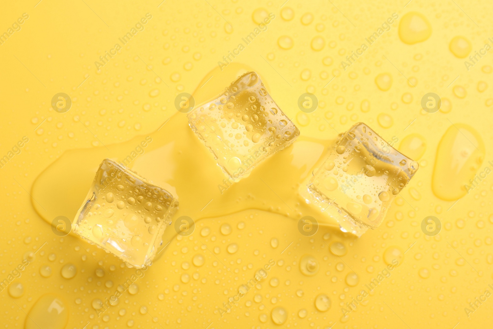 Photo of Crystal clear ice cubes on yellow background, flat lay