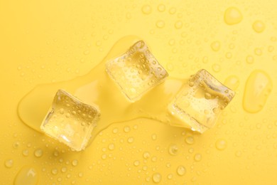 Photo of Crystal clear ice cubes on yellow background, flat lay