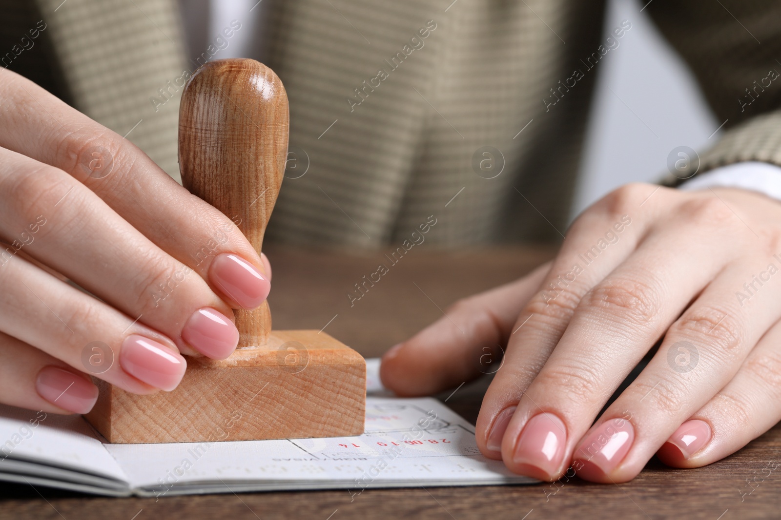 Photo of Ukraine, Lviv - September 6, 2022: Woman stamping visa page in passport at wooden table, closeup
