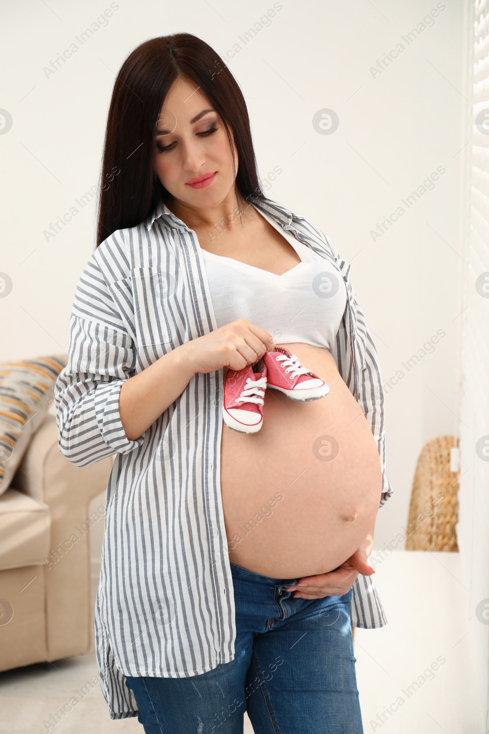 Photo of Beautiful pregnant woman with cute baby shoes at home