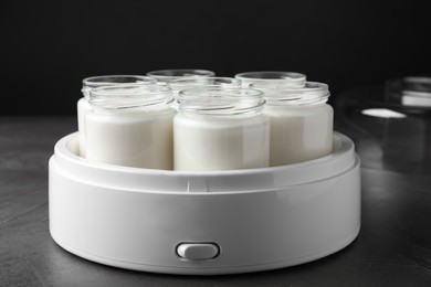 Modern yogurt maker with full jars on grey table