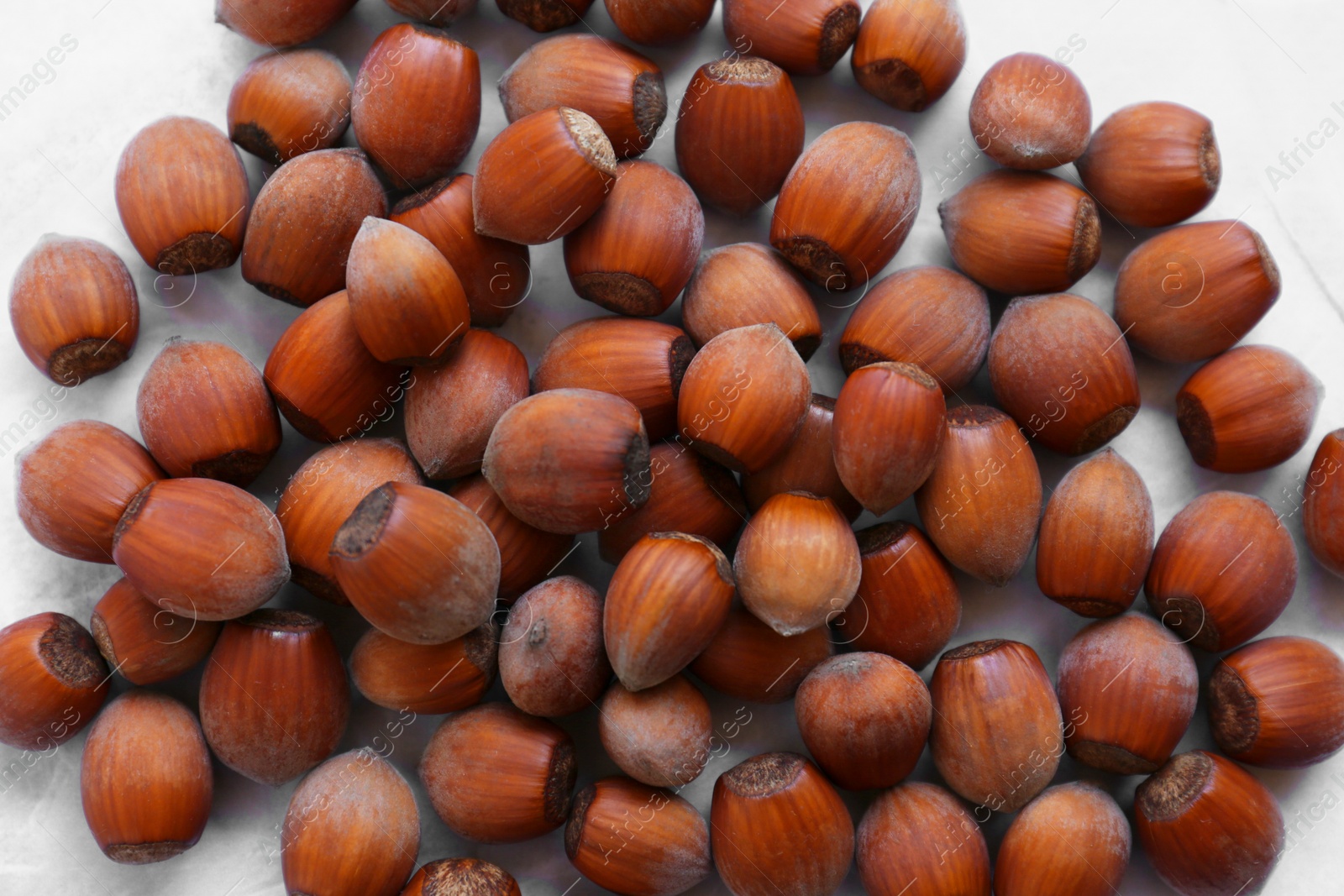 Photo of Pile of tasty hazelnuts on light marble table, closeup