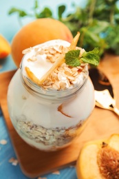 Photo of Tasty peach dessert with yogurt and granola on light blue wooden table, closeup