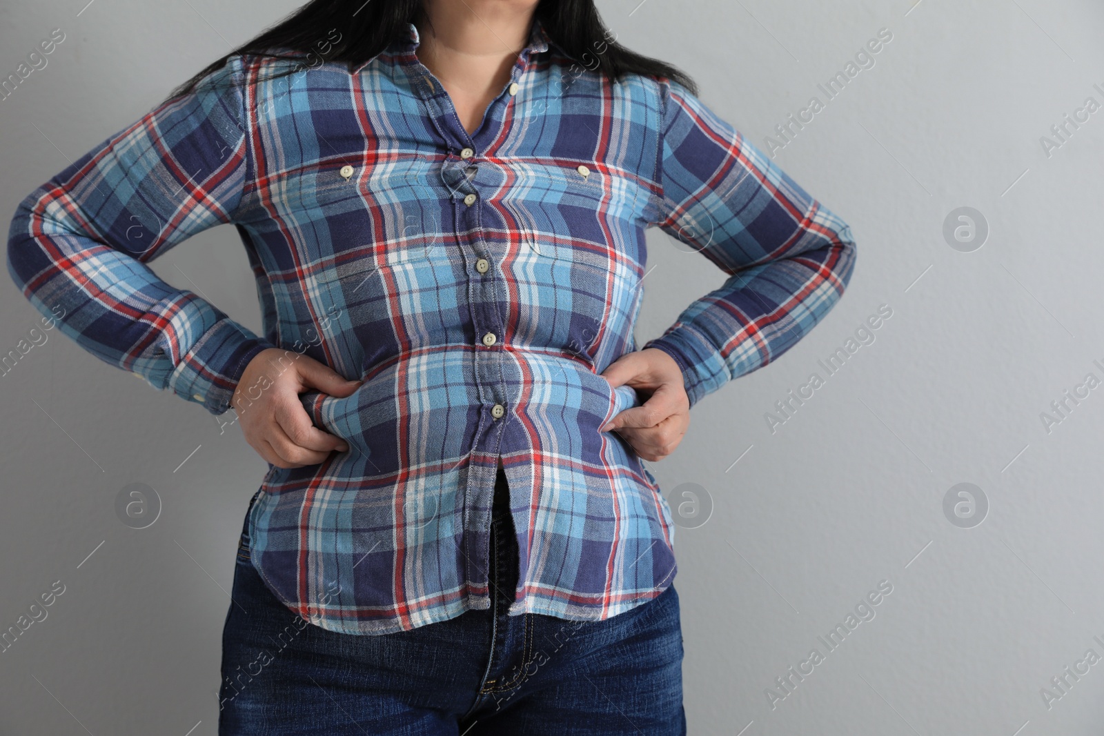 Photo of Overweight woman in tight shirt on light grey background, closeup