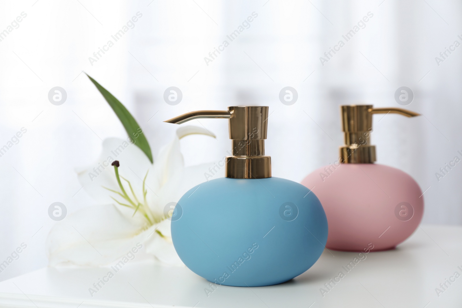 Photo of Stylish soap dispensers and lily on table against blurred background. Space for text