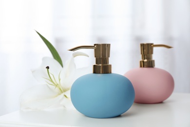 Stylish soap dispensers and lily on table against blurred background. Space for text