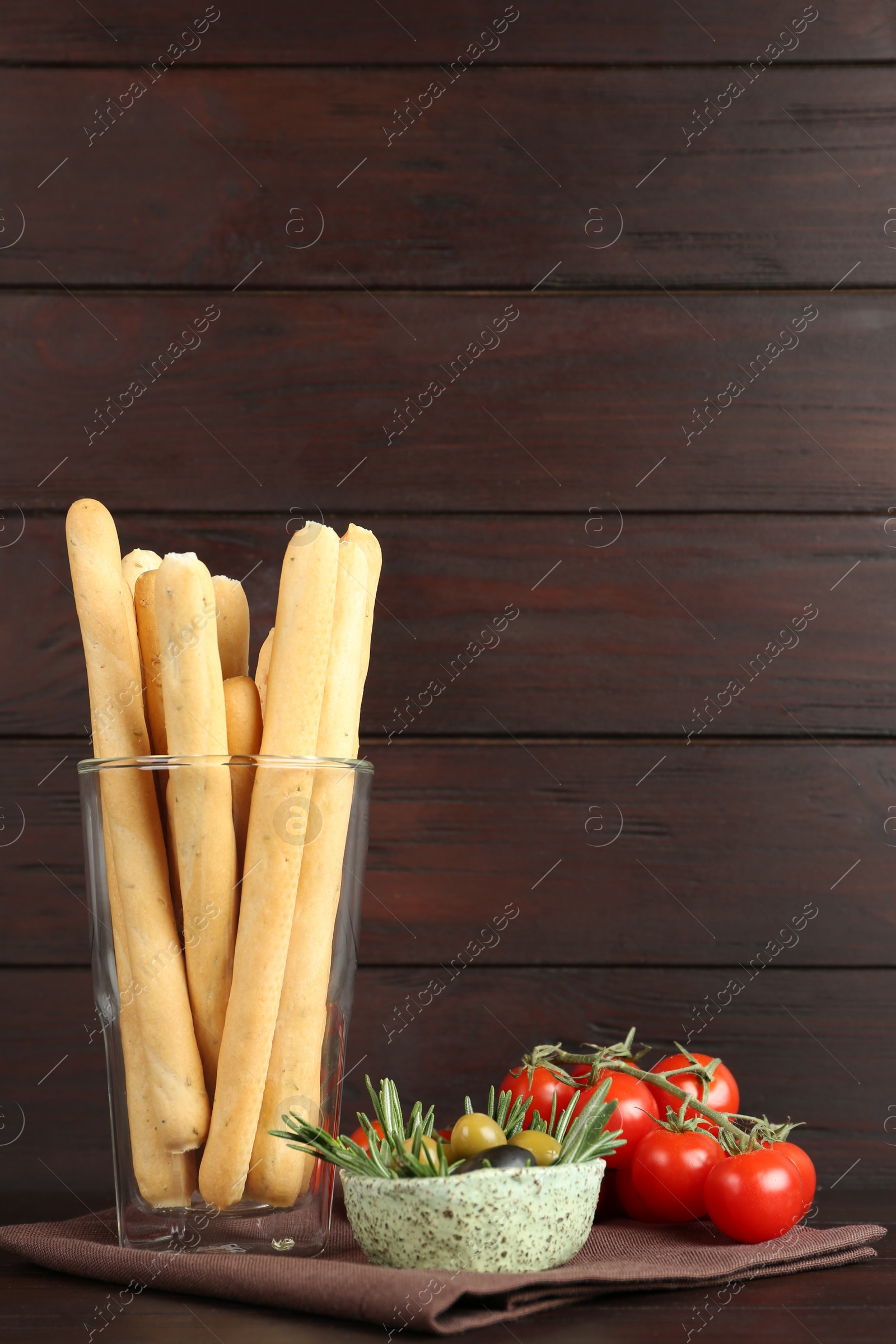 Photo of Fresh delicious grissini in glass, olives with rosemary and tomatoes on wooden table